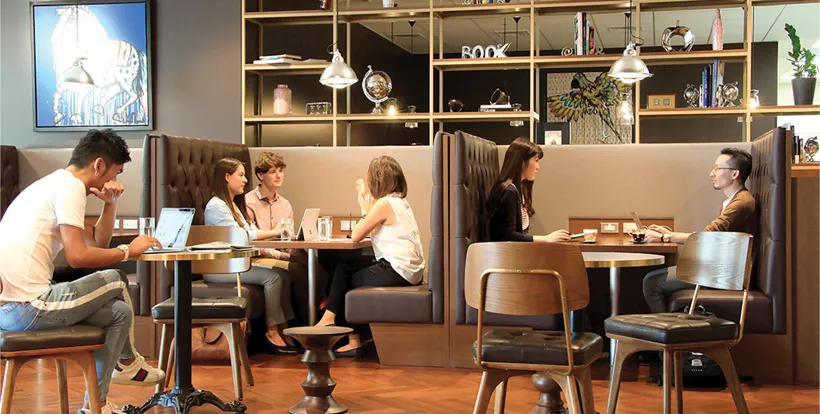 Clients enjoying coffee and working at hot desks in the coworking space at Doha Tower.